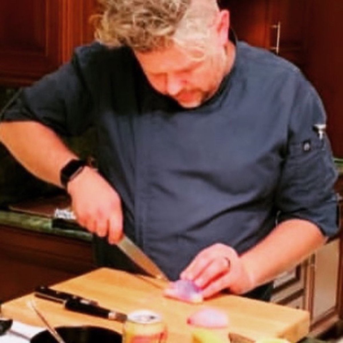 Cutting a shallot on a wooden board at a private catering event, wearing a navy chef coat